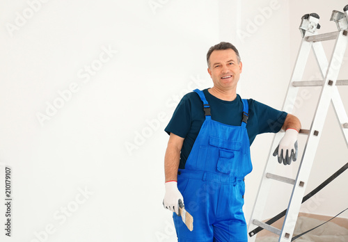 Male painter in uniform with brush near ladder indoors