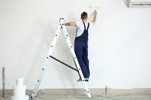 Male painter using roller for refurbishing color of wall indoors photo