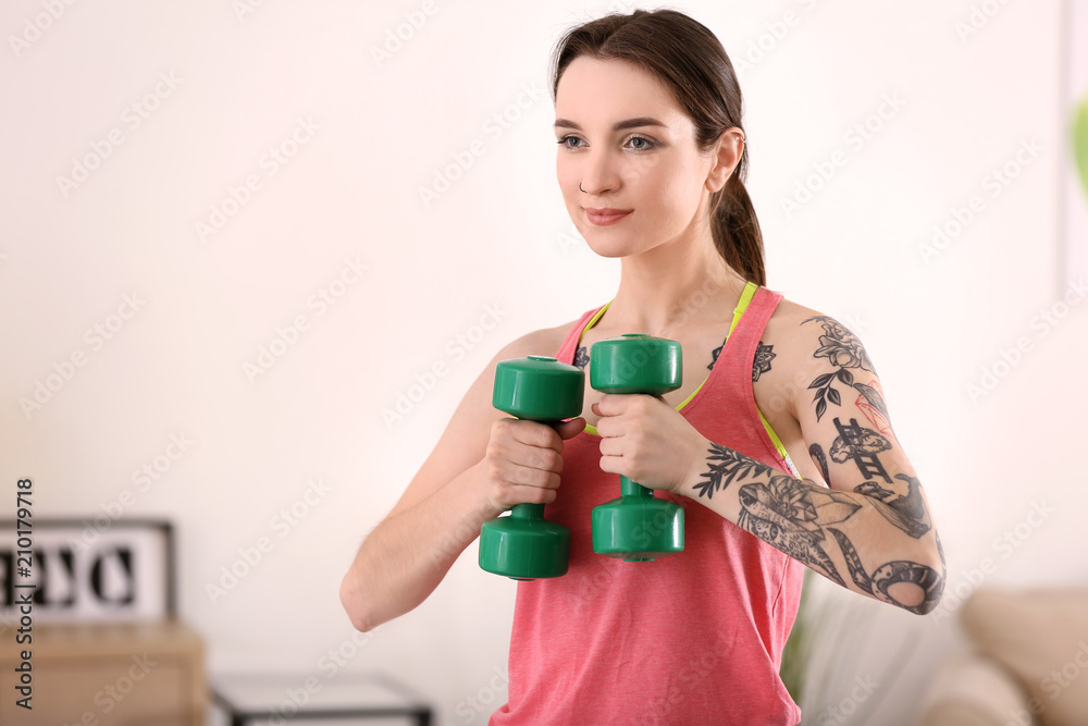 Beautiful young woman doing exercises with dumbbells at home in morning