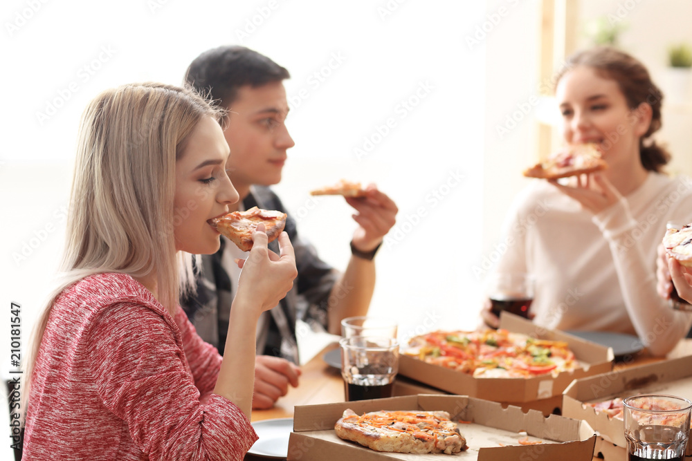 Young people eating pizza at table indoors Young people eating pizza at table indoors