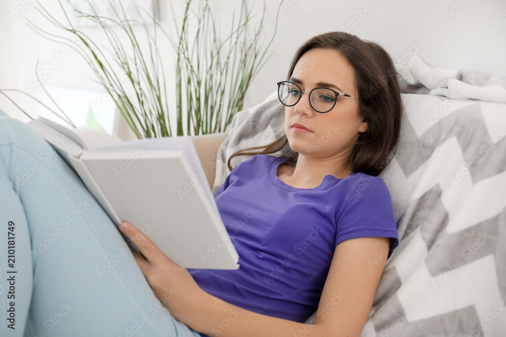Young woman reading book on sofa at home
