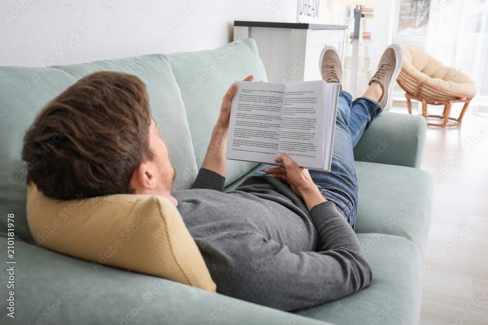 Obraz premium Young man reading book while resting at home