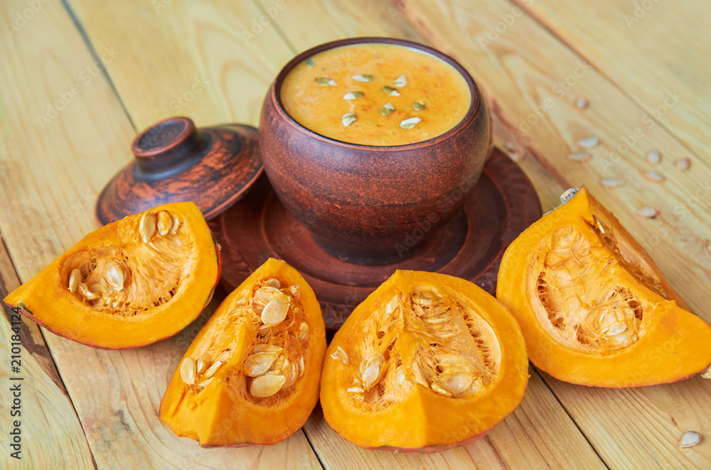 Hot pumpkin soup in a brown bowl decorated with sliced pieces of yellow pumpkin on the wooden background. Traditional autumn food or thanksgiving dish. Side view Hot pumpkin soup in a brown bowl decorated with sliced pieces of yellow pumpkin on the wooden background. Traditional autumn food or thanksgiving dish. Side view