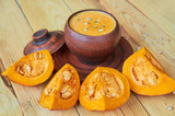 Hot pumpkin soup in a brown bowl decorated with sliced pieces of yellow pumpkin on the wooden background. Traditional autumn food or thanksgiving dish. Side view