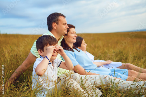 Happy family resting together sitting on grass in summer nature.