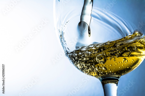 White wine splash on grey background, stream of white wine pouring into a glass. Bright view photo.