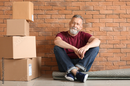 Mature man with moving boxes sitting on carpet at new home
