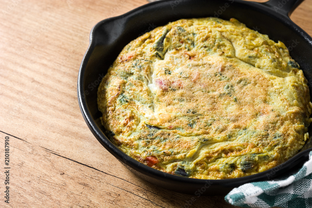 Frittata made of eggs and vegetables in a iron pan, on wooden table. Frittata made of eggs and vegetables in a iron pan, on wooden table.