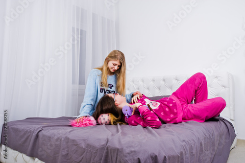 Two friends girls in pajamas having fun on bed at room.