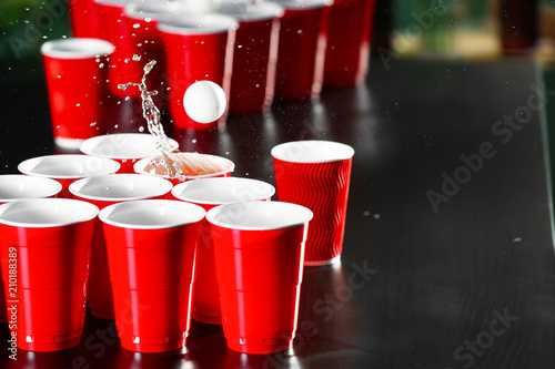 Cups and plastic ball for beer pong game on table photo