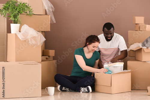 Interracial couple unpacking boxes indoors. Moving into new house