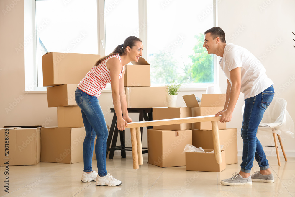 Young couple carrying table in room after moving to new home Young couple carrying table in room after moving to new home