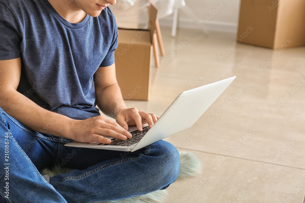 Young man with laptop sitting on floor after moving into new house Young man with laptop sitting on floor after moving into new house