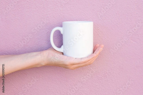 Young Caucasian Woman Holds on Hand Palm Blank Mockup White Mug on Light Pink Painted Wall. Airy Breezy Style. Template for Text Artwork Lettering. Trendy Minimalist Urban Atmosphere