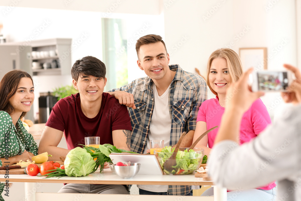 Young man taking photo of his friends in kitchen
