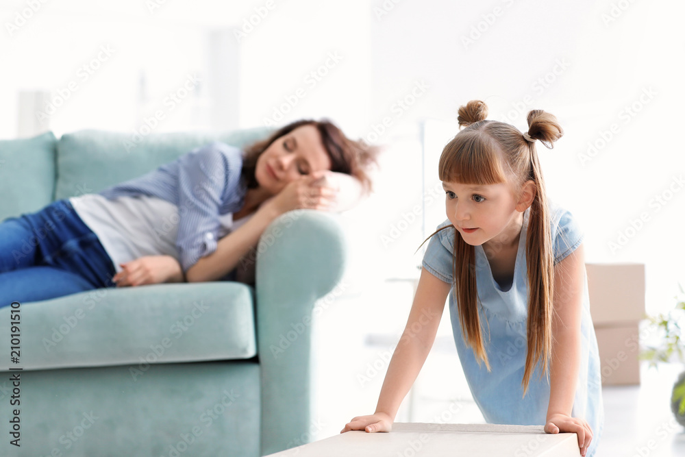 Cute girl with cardboard box and her mother resting on sofa. Moving into new house Cute girl with cardboard box and her mother resting on sofa. Moving into new house