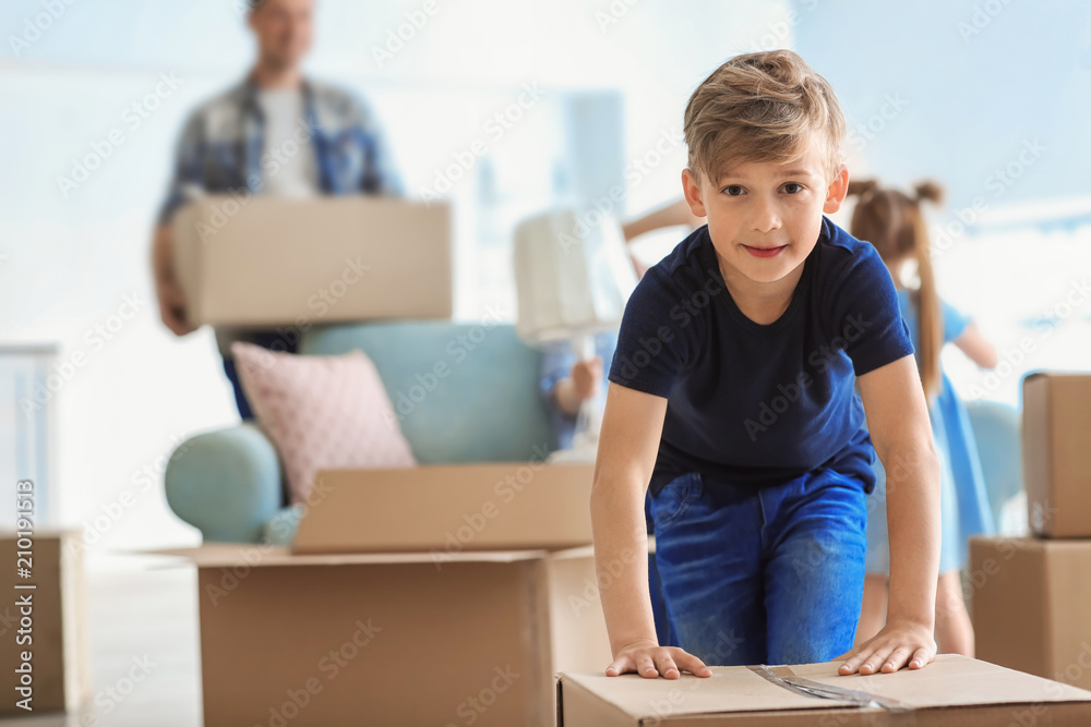 Cute child with box with his family packing belongings at home. Moving into new house Cute child with box with his family packing belongings at home. Moving into new house