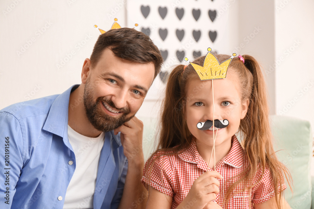 Portrait of smiling father and daughter with artificial mustache and crown at home Portrait of smiling father and daughter with artificial mustache and crown at home