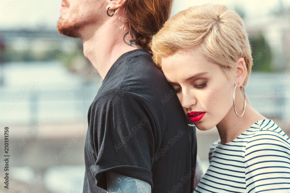 cropped image of stylish girlfriend hugging tattooed boyfriend from back on bridge cropped image of stylish girlfriend hugging tattooed boyfriend from back on bridge