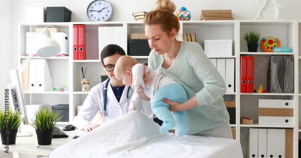 mom undressing child lying on table in doctor office. mom undressing child lying on table in doctor office.