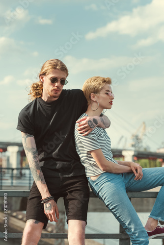 tattooed boyfriend hugging stylish girlfriend on bridge