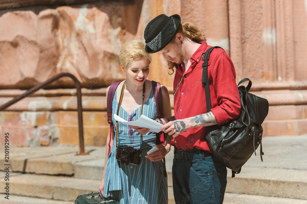 couple of tourists with camera, backpacks and vintage suitcases looking at map