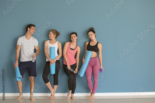 Group of people with yoga mats near color wall