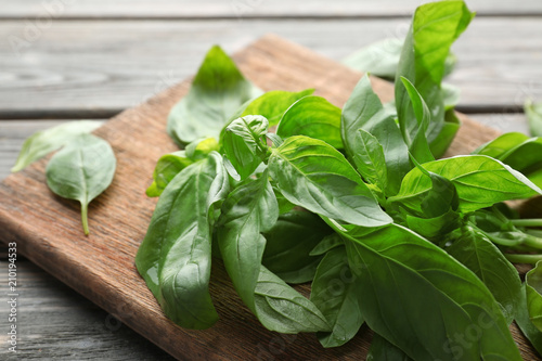 Wooden board with fresh basil on table