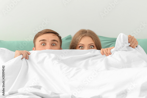 Young couple hiding together under blanket in bed at home