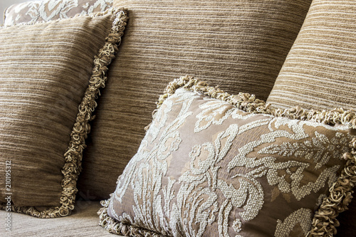 An elegant brown embroidered cushion around normal cushions with yarn edgings, all of them over a couch.
