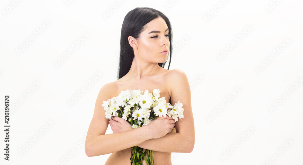 Girl on calm face stands naked and holds chamomile flowers in front of chest. Lady covers breasts with flowers, isolated on white. Woman with smooth healthy skin looks attractive. Skin health concept. Girl on calm face stands naked and holds chamomile flowers in front of chest. Lady covers breasts with flowers, isolated on white. Woman with smooth healthy skin looks attractive. Skin health concept.