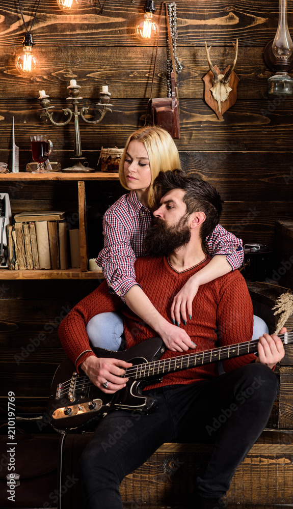 Lady and man with beard on dreamy faces hugs and plays guitar. Romantic evening concept. Couple in love spend romantic evening in warm atmosphere. Couple in wooden vintage interior enjoy guitar music Lady and man with beard on dreamy faces hugs and plays guitar. Romantic evening concept. Couple in love spend romantic evening in warm atmosphere. Couple in wooden vintage interior enjoy guitar music
