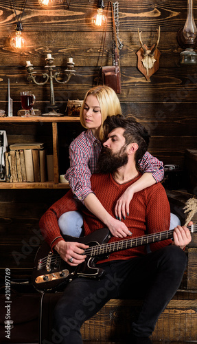 Lady and man with beard on dreamy faces hugs and plays guitar. Romantic evening concept. Couple in love spend romantic evening in warm atmosphere. Couple in wooden vintage interior enjoy guitar music