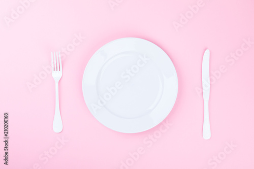 Concept minimal .Time to Eat.  Fork, knife and white Plate on a pink pastel Background. Top View. Flat Lay. Copy space for Text.