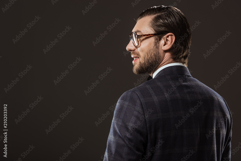 Obraz premium back view of handsome smiling man in eyeglasses looking away isolated on black