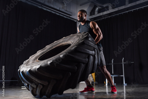 low angle view of muscular african american man training with tyre and looking away