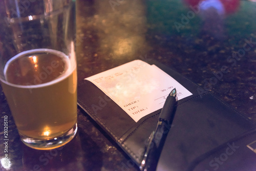 Φωτογραφία Vintage open pint glass beer next to leather bill holder with restaurant check and pen