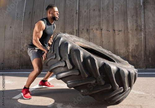 Fototapeta Naklejka Na Ścianę i Meble -  side view of concentrated african american sportsman training with tire on street