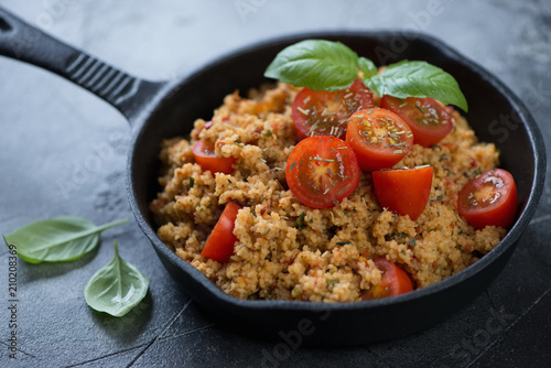 Close-up of a cast-iron frying pan with couscous and cherry tomatoes, studio shot, selective focus