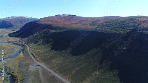 Aerial drone scene of steppe and Nahueve river, epu lauquen, north neuquen, Patagonia Argentina. Gravel road. Camera moving forward on sunny morning. Mountain with shadows, autumn red and yellow trees photo