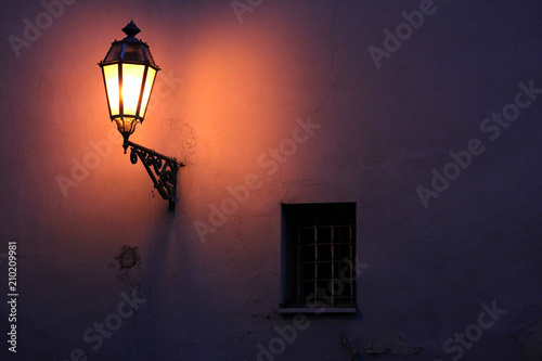 Night view of the illuminated plaster wall with old fashioned street light and window. Old fashioned street light at night.
