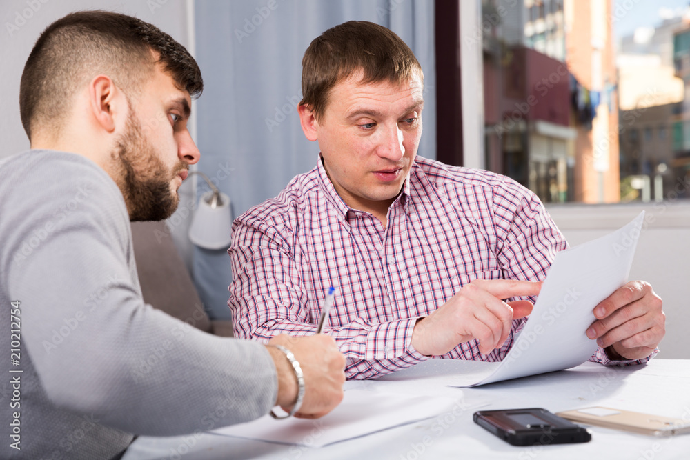 Serious man with friend discussing documents at home table