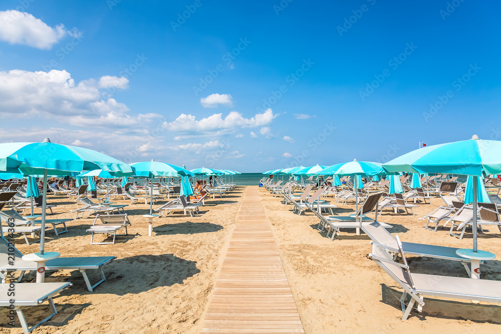 Beach chairs and umbrellas in Rimini, Italy during summer day with blue sky. Summer vacation and relax concept.