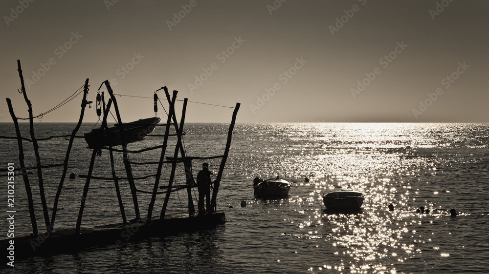 Seascape with boats on the shore and in the sea, silhouette of a man looking reflection on the water, romantic scene