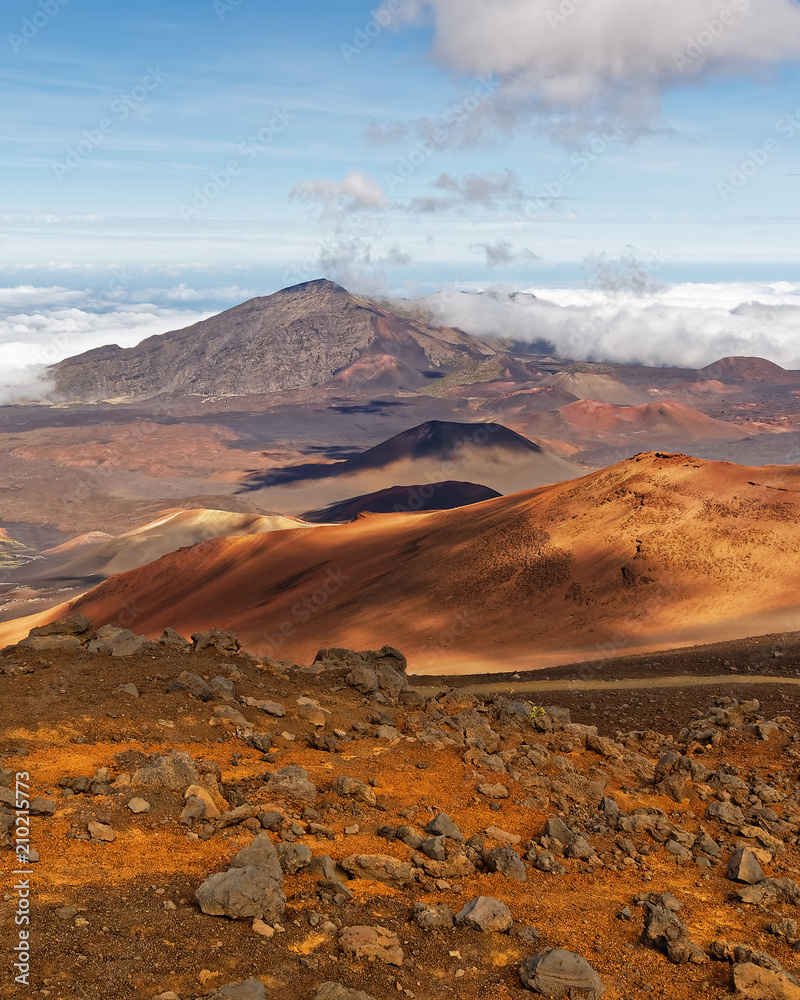 Wide volcanic landscape with lava fields in different colors, wide view, ocher shades, reds, stones in the foreground, cloud shadows, contrast - Location: Hawaii, Island Maui, volcano 
