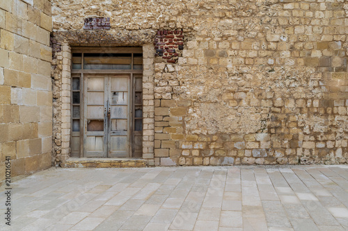 Facade of old abandoned stone bricks wall with broken weathered wooden door © Khaled El-Adawi