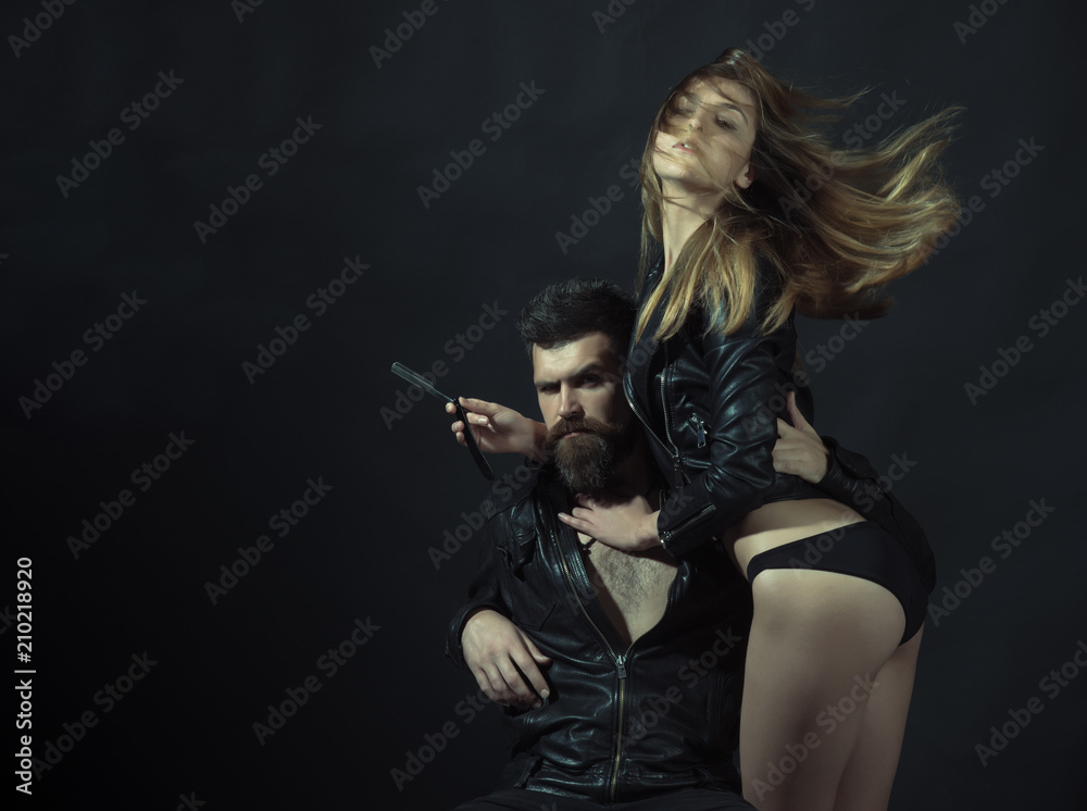 Hipster with beard and sexy girl holds straight razor. Barber with straight razor works on haircut. Couple of sexy girl and brutal bearded hipster with mustache, black background. Barber concept Hipster with beard and sexy girl holds straight razor. Barber with straight razor works on haircut. Couple of sexy girl and brutal bearded hipster with mustache, black background. Barber concept