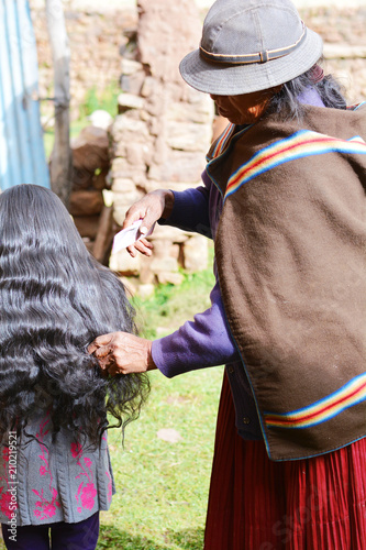 Native american grandmother combing hair of her granddaughter in the countryside.