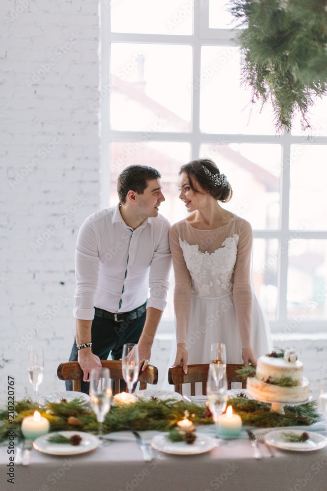 Emotional beautiful newlywed couple smiling, kissing and hugging at wedding reception in white hall with wedding decorations Emotional beautiful newlywed couple smiling, kissing and hugging at wedding reception in white hall with wedding decorations
