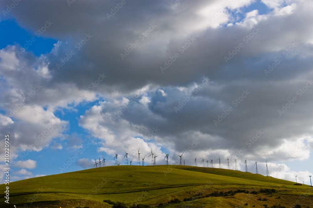 Grey and White Cloudy Blue Sky With Green Rolling Hills & Windmills Grey and White Cloudy Blue Sky With Green Rolling Hills & Windmills